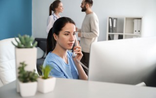 Female medical receptionist on phone will colleagues talking in background
