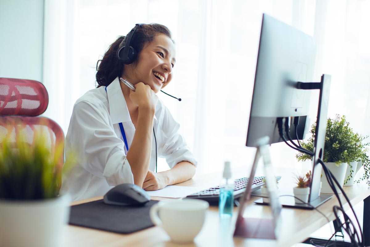 8×8-offer-page_2 Girl with headset smiling and looking at desktop computer