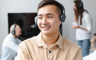 Young man in office wearing headset and smiling with colleagues in background
