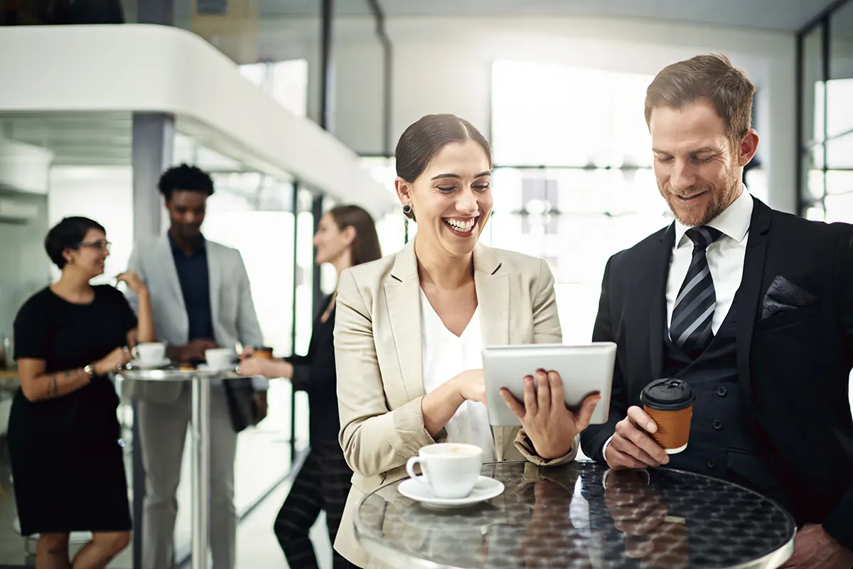 Colleagues gathered in a communal area, two of them looking at a tablet device and smiling
