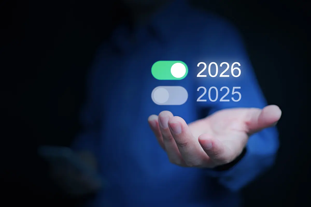 Person in blue shirt holding a smartphone and presenting a digital overlay with toggle switches for years 2025 and 2026, symbolizing future planning and technological transition.